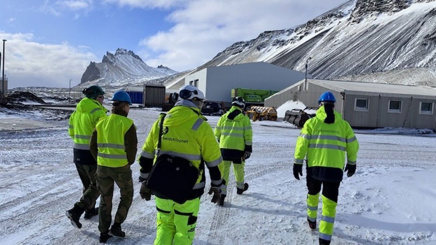 Personer kledd i gult arbeidstøy avbildet i snødekte omgivelser på Jan Mayen.