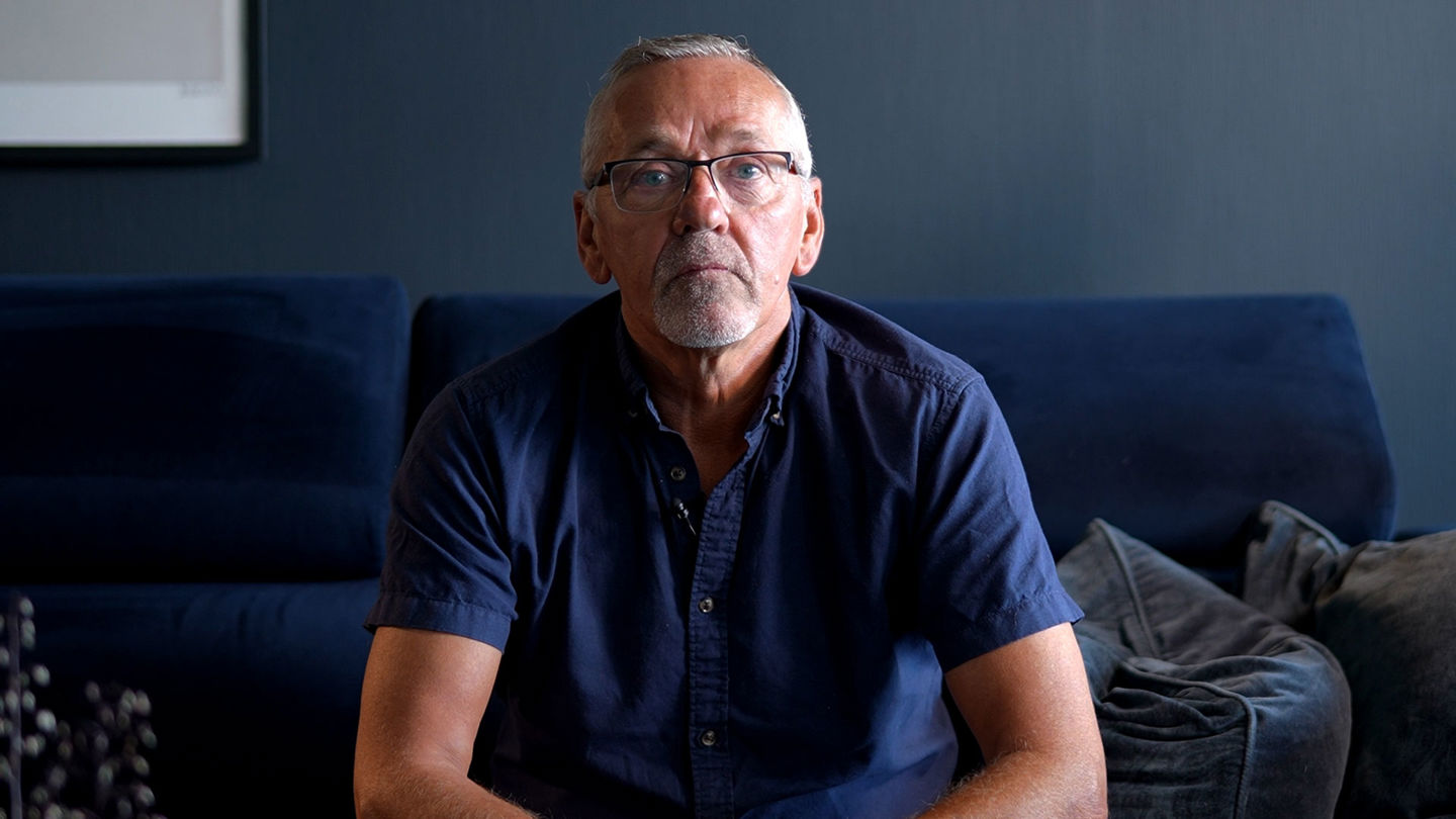 Roy Amundsen sitter foroverlent i en blå sofa og ser rett i kamera med en alvorlig mine