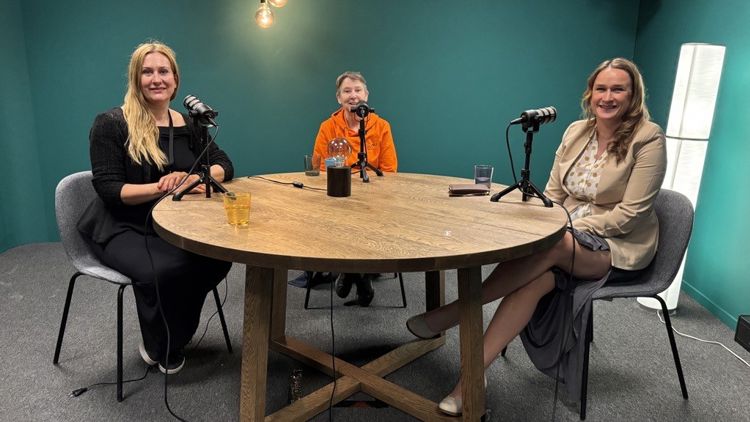 Bilde fra en podkaststudio der tre kvinner sitter rundt et bord med hver sin mikrofon foran seg.