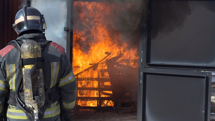 Brannmann i uniform med ryggen til kamera ser på flammer i et hus