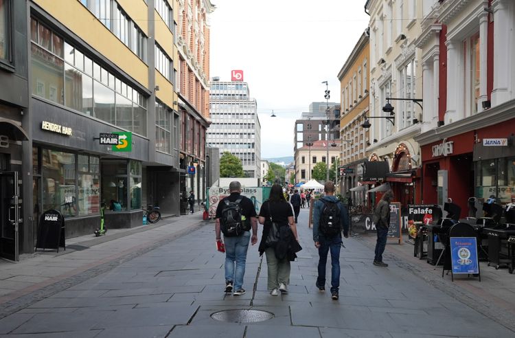 To menn og en kvinne fotografert bakfra mens de  spaserer i en gate med mange bygninger rundt.