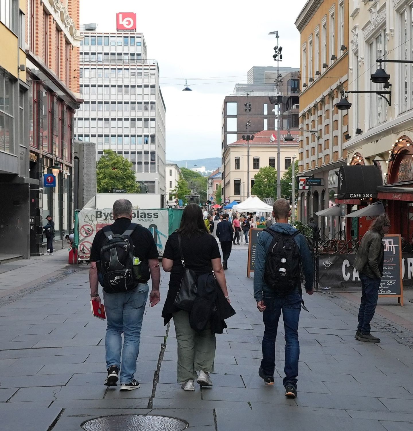 To menn og en kvinne fotografert bakfra mens de spaserer i en gate med mange bygninger rundt