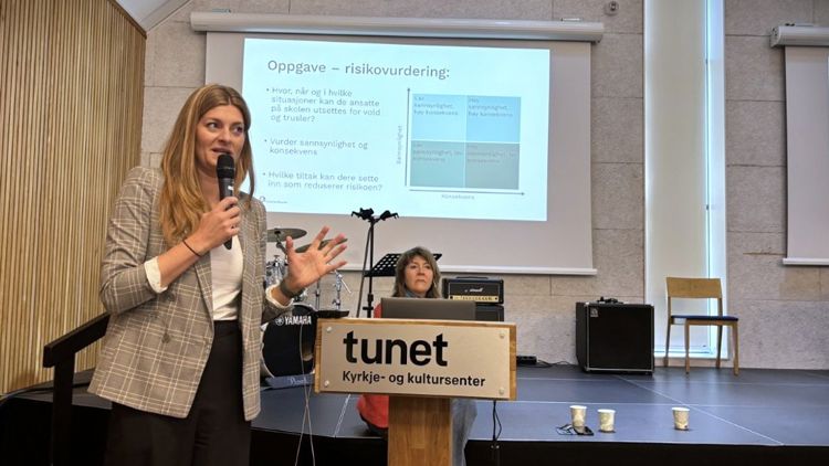 Kvinne som snakker i en mikrofon foran en powerpoint-presentasjon