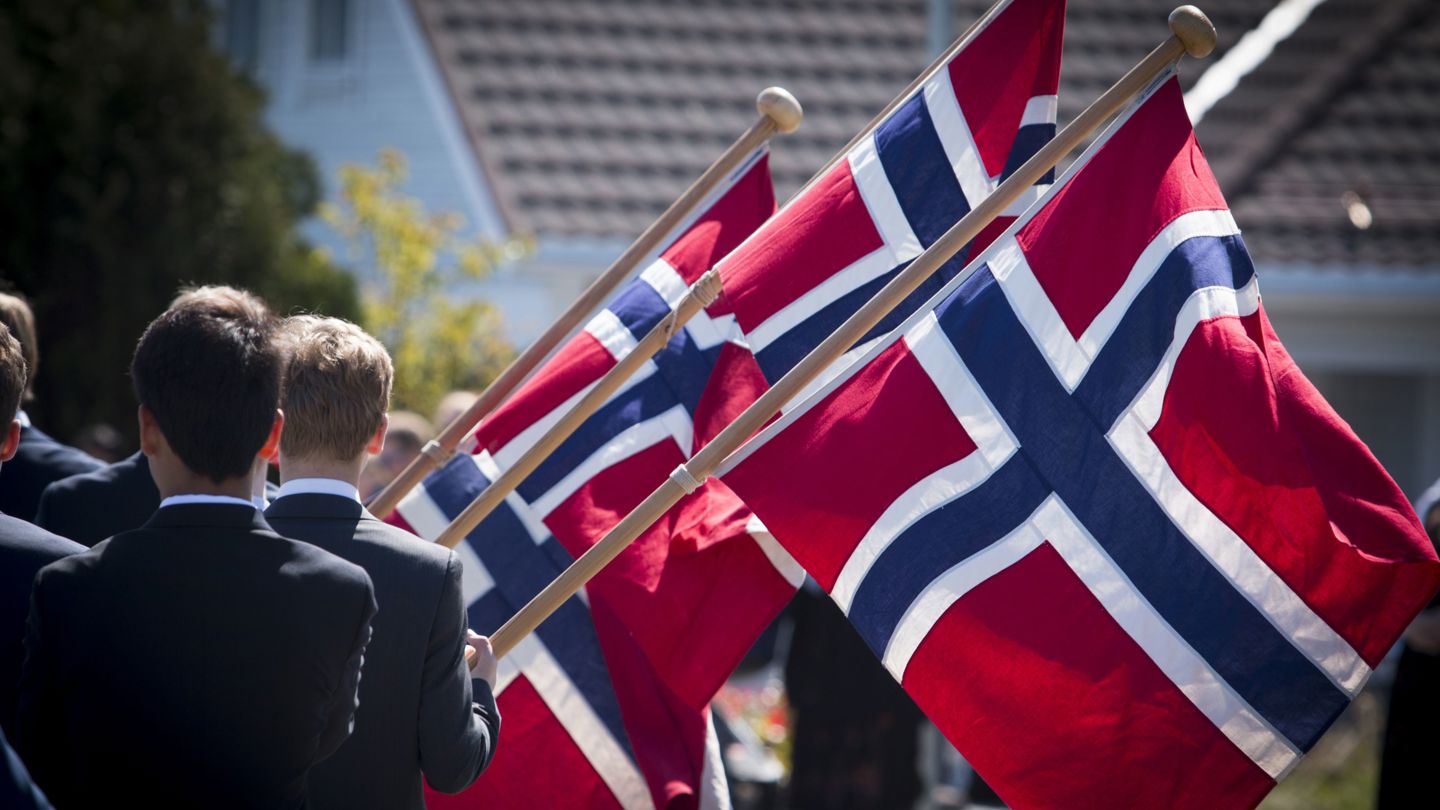 Bildet viser gutter som går i 17. mai-tog og holder i norske flagg.