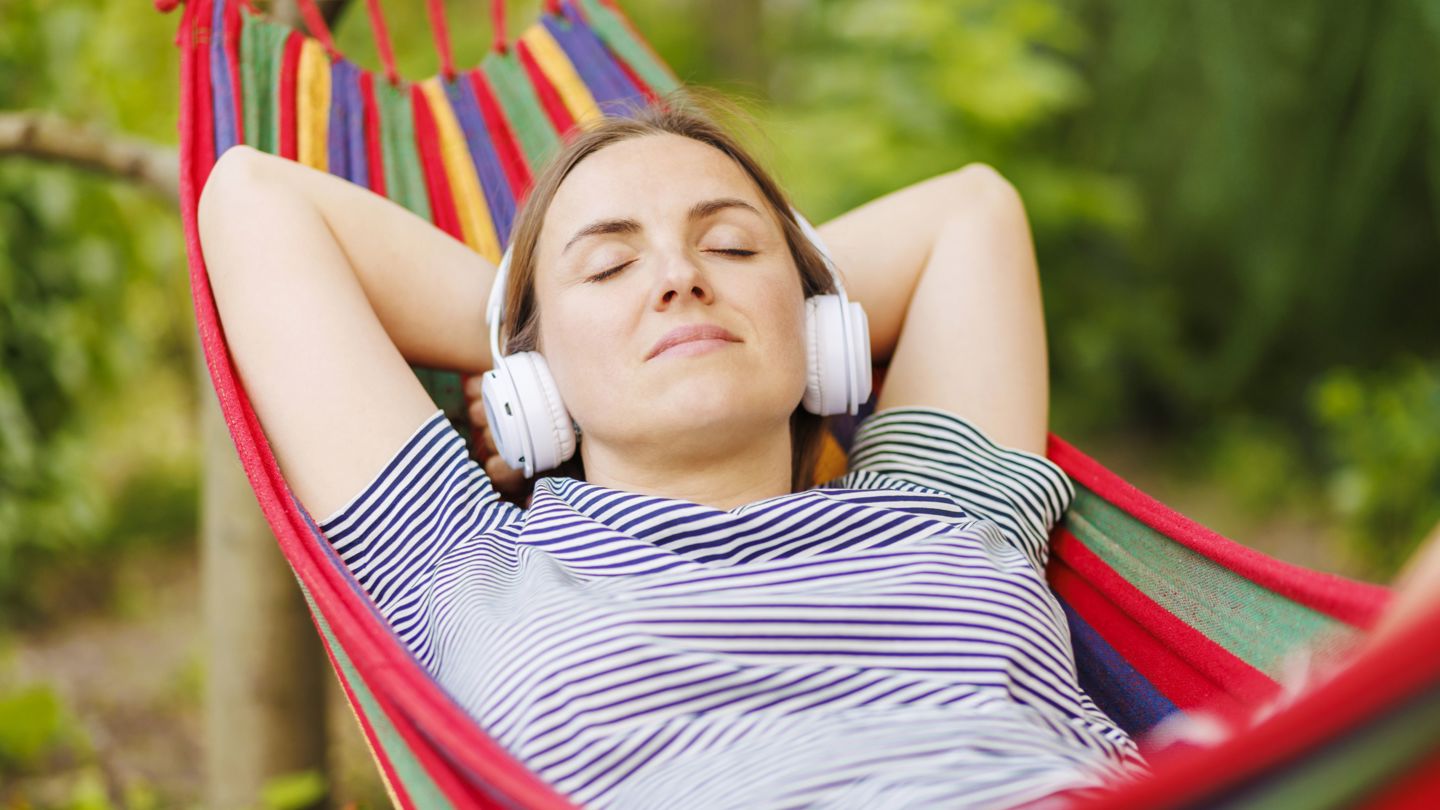 Bildet viser en kvinne som ligger i en hengekøye med headset. 
